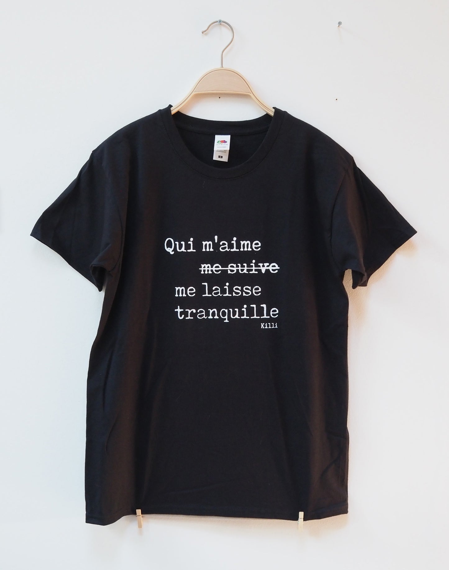 Black t-shirt with white text in french on a hanger against a white background