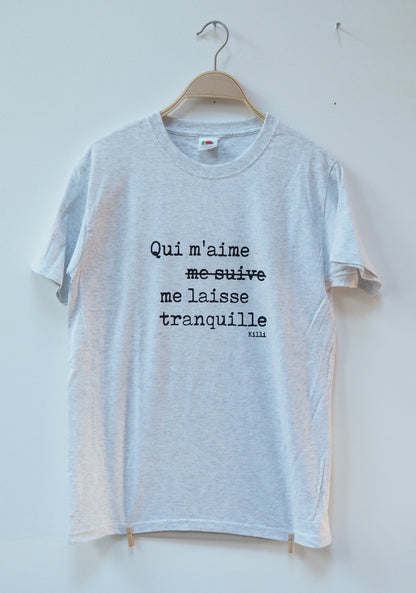 Gray t-shirt with French quote on a hanger against a white wall