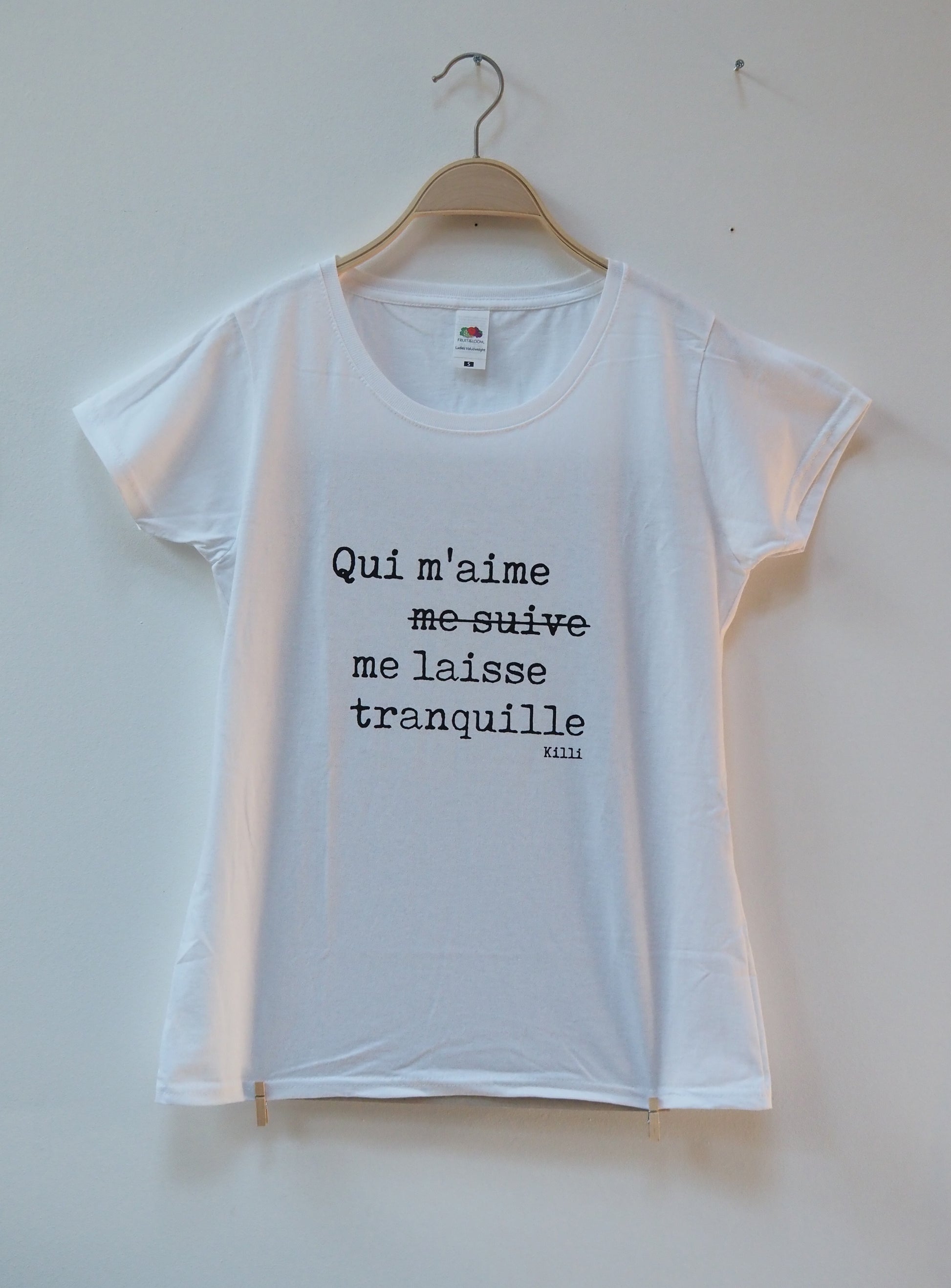 White t-shirt with french quote on a hanger against a white wall